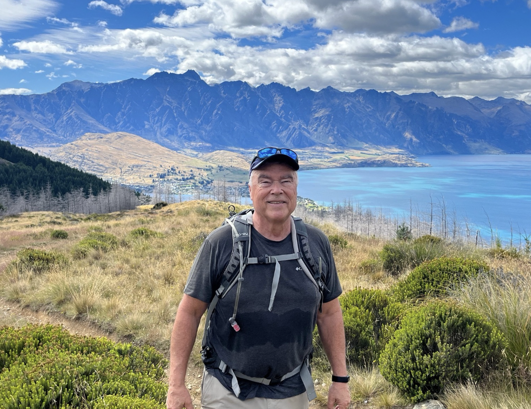 Jim Snipes hiking in New Zealand with Lake Wakatipu and The Remarkables mountain range in the background
